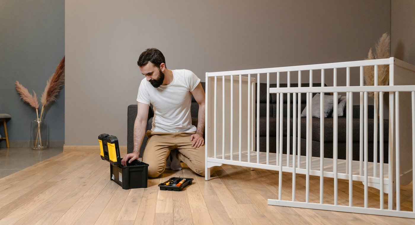 Handyman kneeling beside a toolbox while assembling a white crib