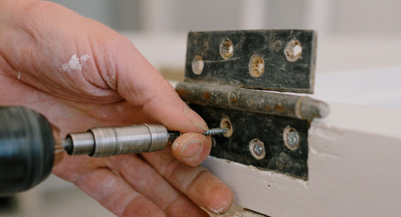 A hinge being screwed onto a white-painted door frame