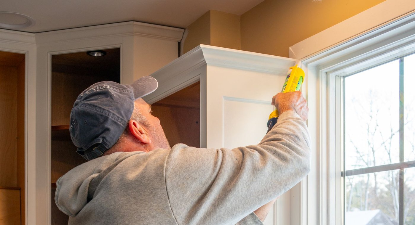 Running a bead of caulk where a cabinet's crown molding meets a window casing