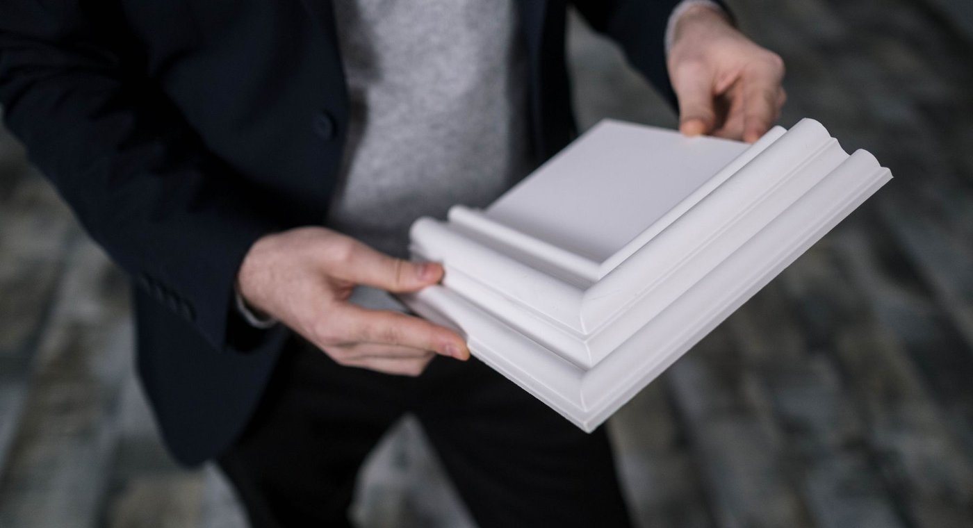 Hands holding white crown molding and baseboard samples